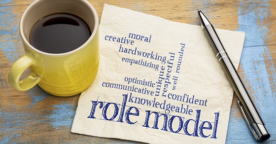 A cup of coffee sits on a napkin with words written on it like role model, knowledgeable, confident, and communicative.