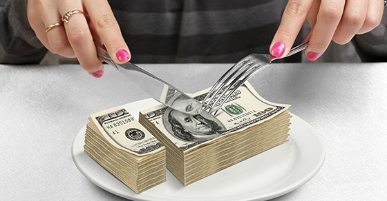 A person cuts up a stack of hundred dollar bills with a knife and fork like they are eating a piece of cake. It symbolizes how a bad apportionment clause can mess up an estate plan.