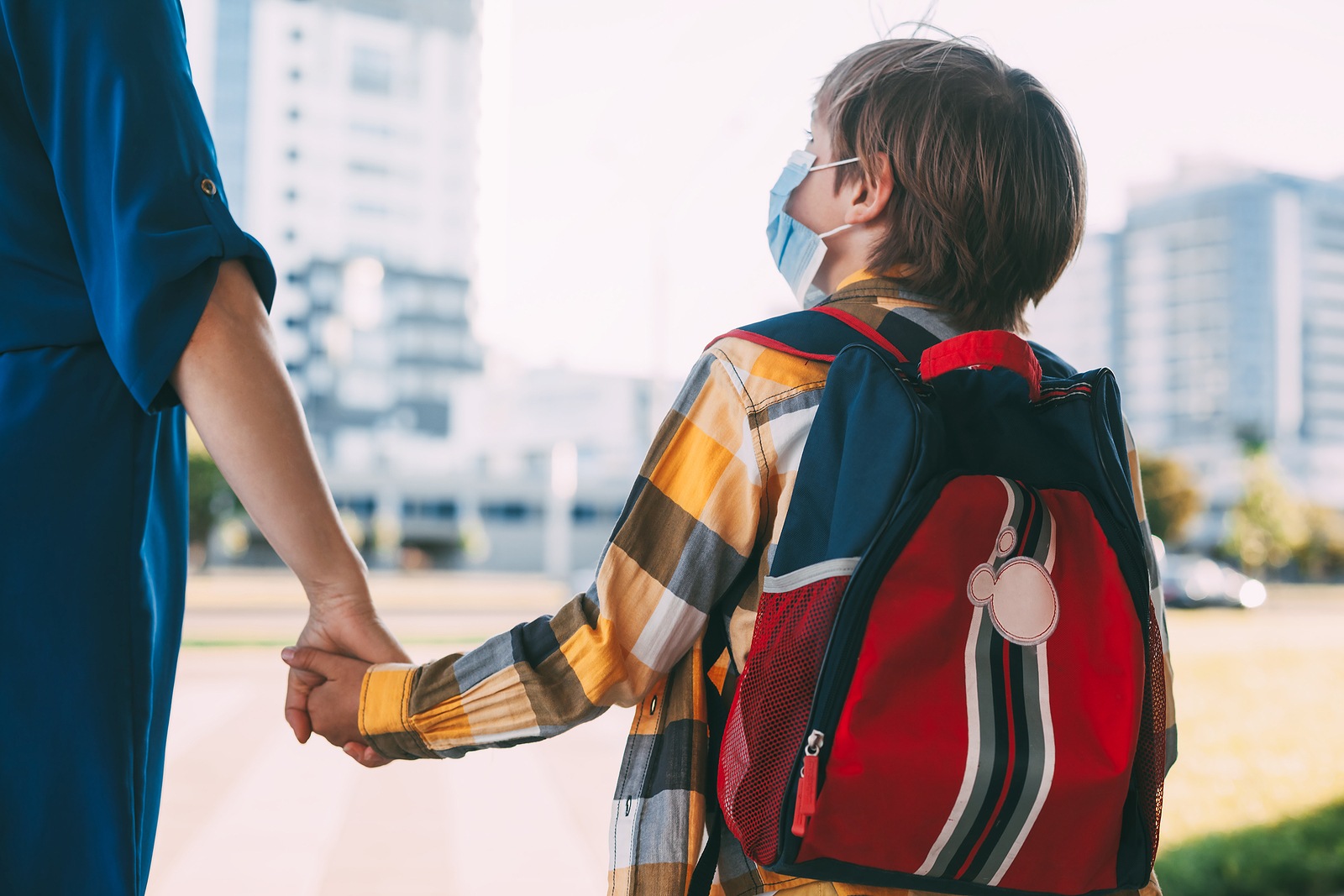 A child wearing a mask is walking with one of their parents.