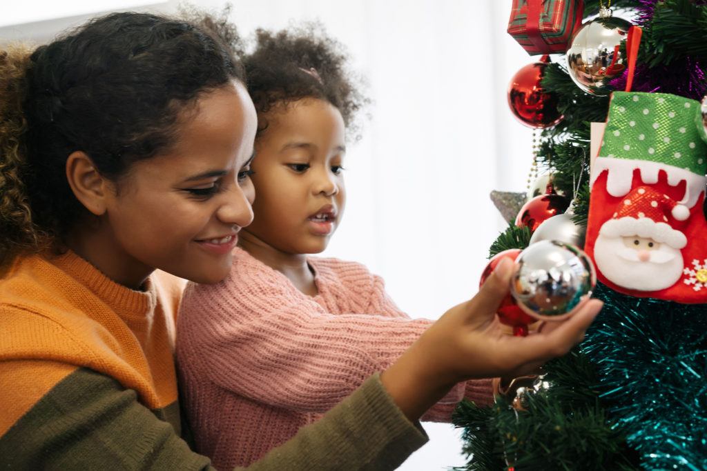 A mother and her daughter are hanging Christmas tree ornaments.